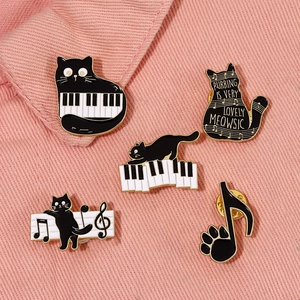 Niedliche Emaille-Pins Set mit schwarzen Katzen und Klaviertasten auf Denim-Hintergrund