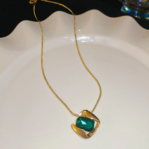 Detailed shot of a green square gemstone pendant on a gold snake chain necklace