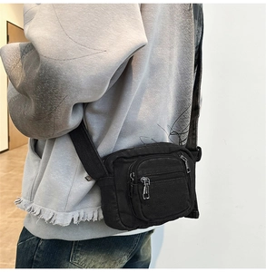 Detail shot of the black canvas mini crossbody bag worn by a model in casual streetwear style