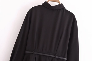 Detail of black long-sleeved dress with lapel collar and matching belt on wooden hanger