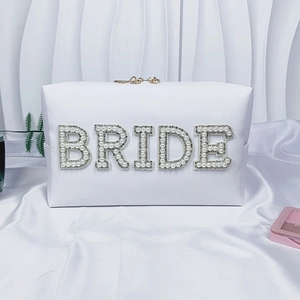 Detailed view of pearl and rhinestone BRIDE lettering on a white faux leather makeup bag