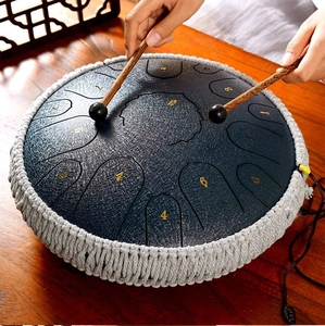 Deep grey steel tongue drum with woven rope detail on wooden table being played with mallets