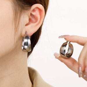 Polished silver chunky U-shaped stainless steel hoop earrings on ear and held by model hand