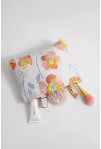 Detail of 3D orange floral embroidery and yellow tassel on a cotton cosmetic bag