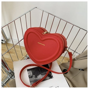 Détail du sac à bandoulière rouge en cœur avec logo doré et fermeture éclair chic