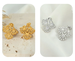 Detail of pine branch stud earrings in gold and silver finish on textured backgrounds