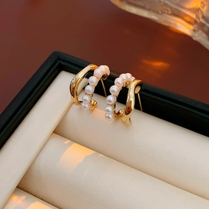 Detailed close-up of golden C-shaped double-layer earrings with small pearls in a jewelry box