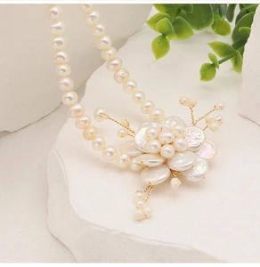 Macro shot of baroque pearl flower pendant with gold wire on white marble background