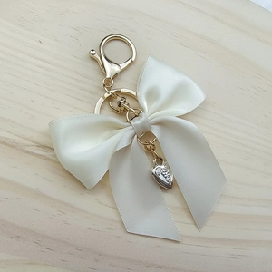 Detail of white ribbon bow keychain with golden heart pendant on wood texture