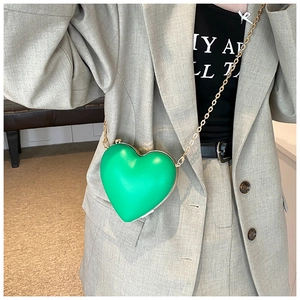 Close-up of heart-shaped green crossbody bag with gold chain on grey blazer