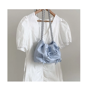 Detail of light blue shoulder bag with pleated bows and silver chain strap on dress