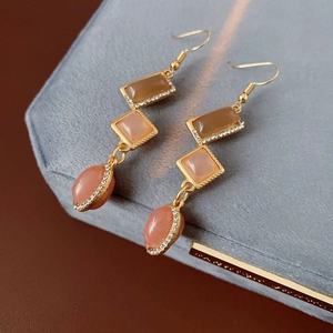 Close-up of vintage gold drop earrings with tiered geometric gems on grey velvet display