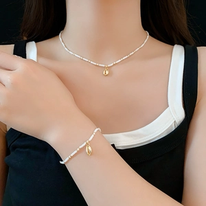 Detail of bohemian necklace and bracelet set with white beads and gold conch shell charms