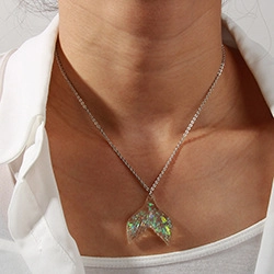 Close-up of a silver necklace featuring an iridescent mermaid tail pendant on a model