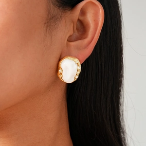 Fashionable oval pleated gold earring with white inlay and crystals worn by a model