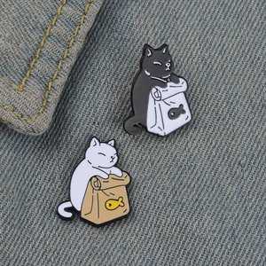 Set of two cute black and white cat enamel pins in paper bags on denim background