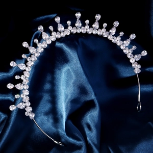 Close-up of a silver tiara with sparkling teardrop crystals on blue satin fabric
