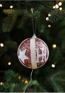 Pink sequined Christmas ornament with white velvet stripes hanging on a green tree