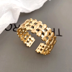 Macro detail of gold-plated woven hollow open bangle with layered drop-shaped metal texture
