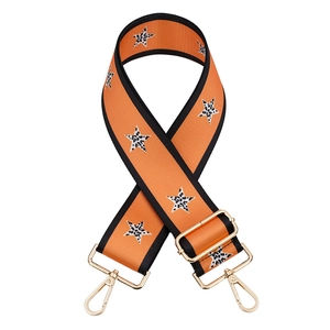 Close-up of orange bag strap with leopard star patterns and gold metal buckles