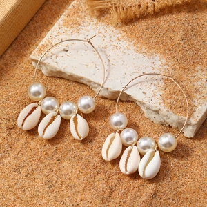 Golden hoop earrings with white pearls and shells on a sandy beach vacation background