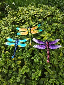 Detailed view of colorful metal dragonflies on green leaves showing vibrant painted patterns