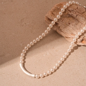 Detail of elegant pearl necklace with a matte silver curved metal bead on a warm surface