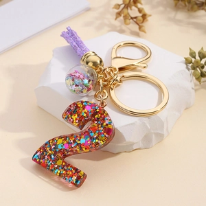 Detail of resin number 2 keychain with sequins, purple tassel and glass ball