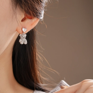 Vue détaillée de boucles d'oreilles cœur argenté avec pendentif ours en cristal sur l'oreille