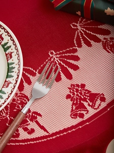 Close-up of red Christmas lace tablecloth with bell and bow patterns on a wooden table