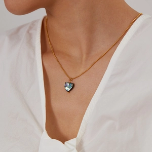 Close-up of heart-shaped abalone shell pendant necklace on golden bead chain worn by model