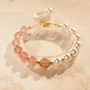 Detailed shot of strawberry quartz and pearl bracelet with gold hardware on clear stand