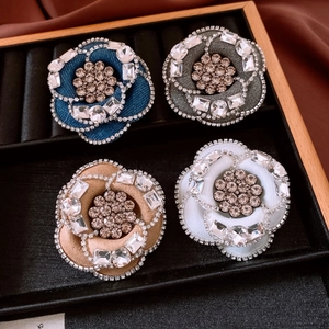 Macro view of four camellia fabric brooches with rhinestone accents on a black velvet tray