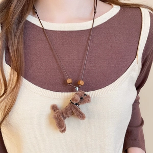 Detail of plush brown teddy dog pendant with beads on model wearing knit sweater