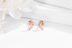 Detailed view of crescent moon stud earrings in rose gold finish on white flower