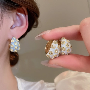 Detailed view of C-shaped white enamel hoop earrings with gold floral crystal studs