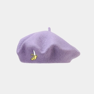 Dettaglio di un basco in lana viola con ricamo a forma di banana gialla sul lato