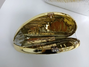 Detalle de bolso de noche tipo concha dorada abierto con bisagra interna y cierre de strass