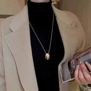 Close-up of a gold teardrop pendant necklace worn by a model over a beige coat and black top