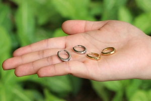 Detail of silver and gold U-shaped hoop earrings held in hand against natural background