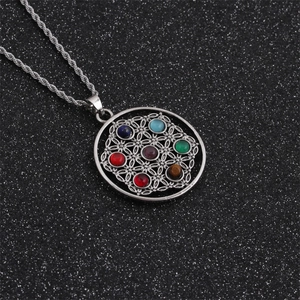 Close-up of a silver hollow geometric pendant with seven colorful chakra gemstones