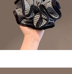 Détail d'un grand chouchou à carreaux noirs et blancs tenu à la main pour l'échelle