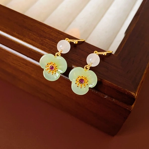 Detail of gold-plated flower earrings with green petals and pearls on a wooden tray