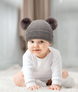 Close-up of a baby wearing a dark grey ribbed knit beanie with two soft fur pom-poms