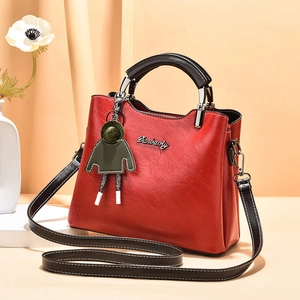 Red oil wax PU leather handbag with black handles and a cute green charm on beige background