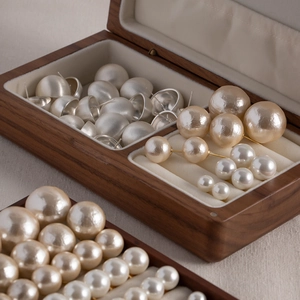 Walnut wood jewelry box displaying assorted brushed metal earrings and pearls