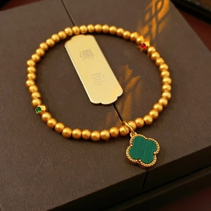 Detailed shot of 18k gold plated bracelet with green clover and engraved gold coin charm