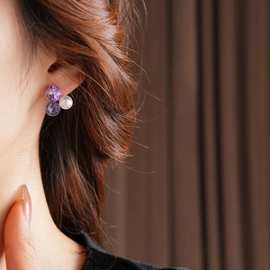Detail view of triangle earrings with purple crystals and white pearl on earlobe