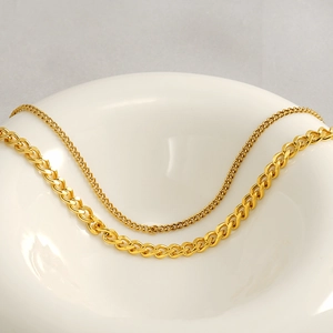 Golden stainless steel Cuban and cross link chain necklace set on white ceramic plate