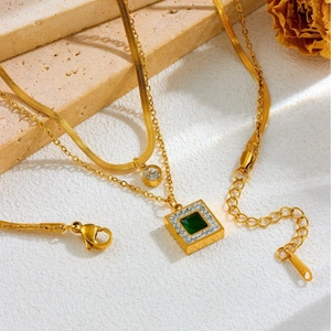 Close-up of a double-layer gold snake chain necklace with an emerald pendant on stone
